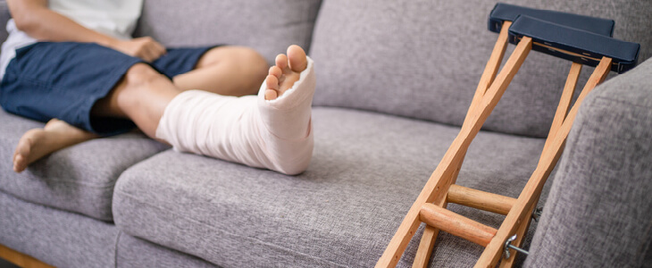person with broken foot laying on the couch with a cast and crutches