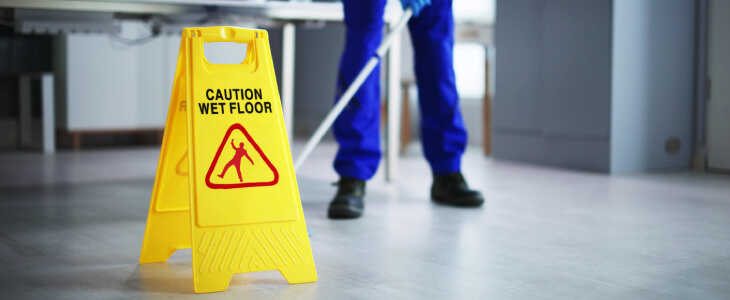 Janitor mopping floors in an office with a "CAUTION - WET FLOOR" sign