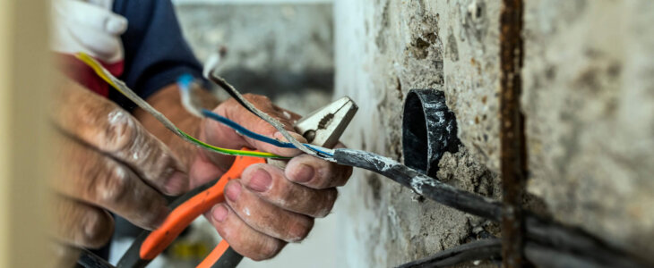 Photo of Electrician peeling off insulation from wires - closeup on hands and pliers. electrician binding copper wires together and sealing them with insulation stripe. Man mounting the wires into electrical wall fixture or socket - closeup on hands and pliers.