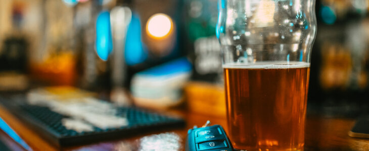 Close up image depicting a partially consumed pint of beer next to a set of car keys on the bar counter, illustrating a drunk driving concepts. Room for copy space.